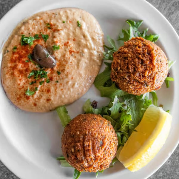 Two falafel balls, hummus with an olive, lettuce, and a lemon wedge on a white plate.