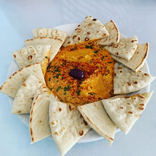 A plate of Athena Gyro's hummus with a single olive and pita bread triangles.