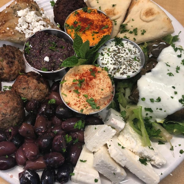 A Greek platter with feta, olives, meatballs, pita, and various dips like hummus and tzatziki.