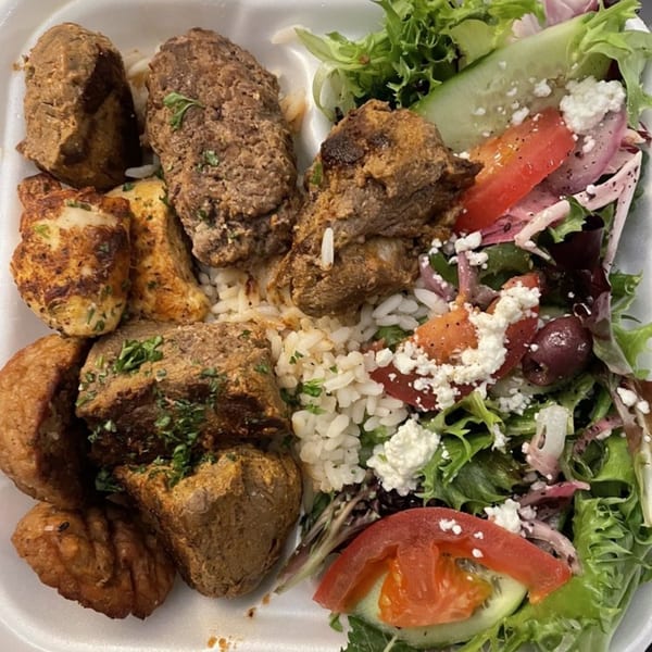 A Greek platter with meat, rice, roasted potatoes, and a fresh salad with feta and olives.