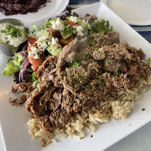 Athena Gyro's Greek dish with shredded meat over rice, a side salad, and tzatziki sauce.