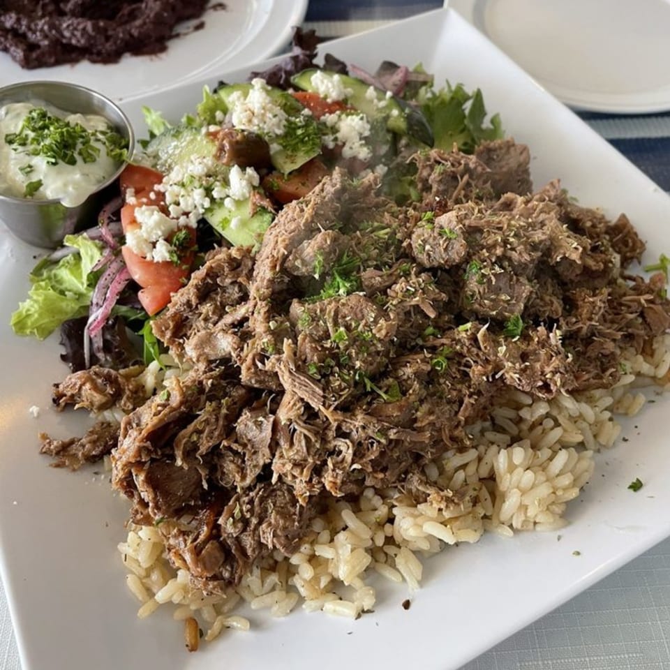 Athena Gyro's Greek dish with shredded meat over rice, a side salad, and tzatziki sauce.